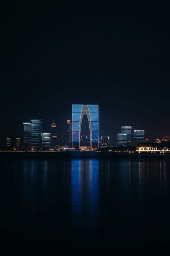Illuminated buildings by river against sky at night