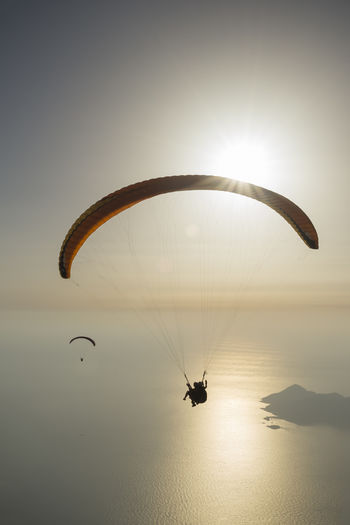 Distant view of people paragliding over sea during sunset