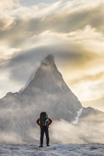 Climber standing in front of mt. loki, baffin island, canada.