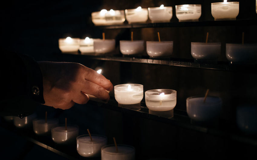 Cropped image of person igniting tea lights on shelf at church