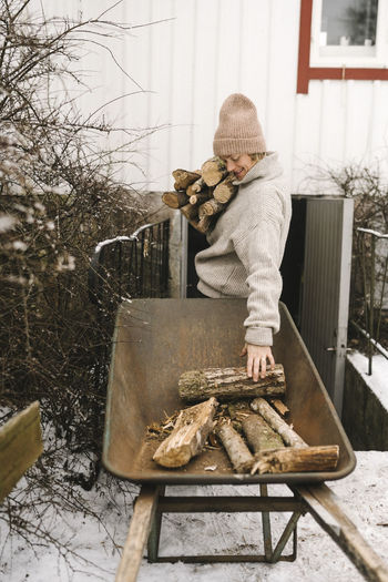 Woman collecting firewood from wheelbarrow during winter