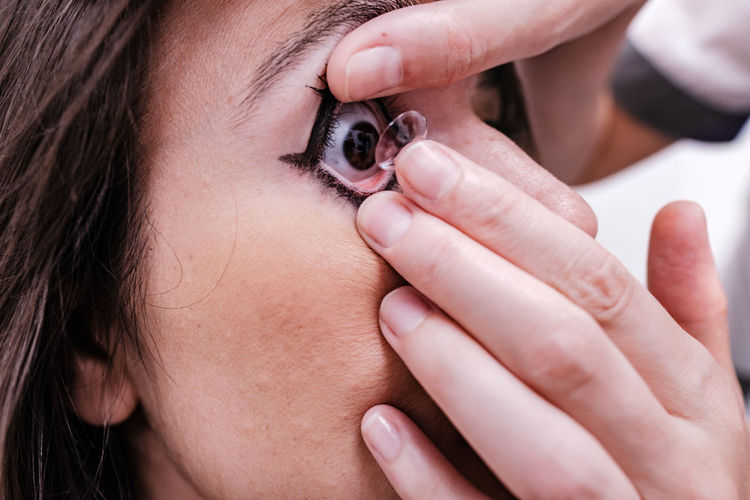 Crop anonymous female ophthalmologist putting contact lens on eye of woman during appointment in modern hospital