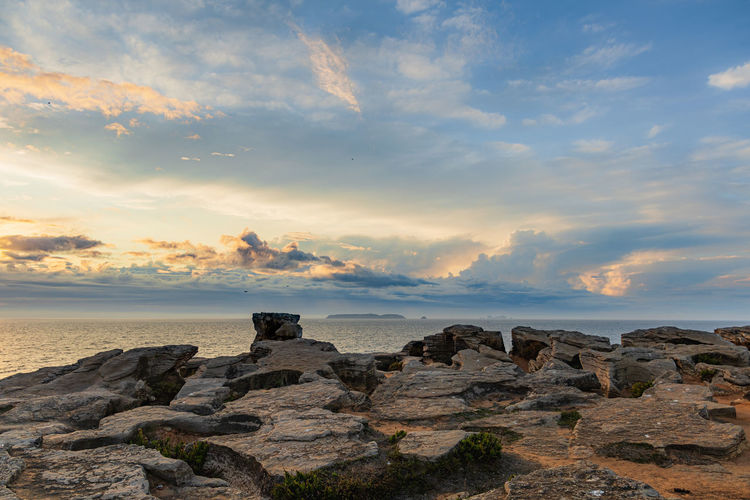 Rocks on shore against sky during sunset