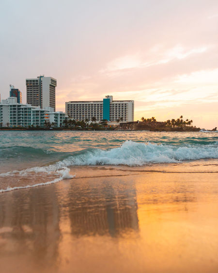 Sunset sky with buildings reflection in sand and waves in a city beach of condado puerto rico