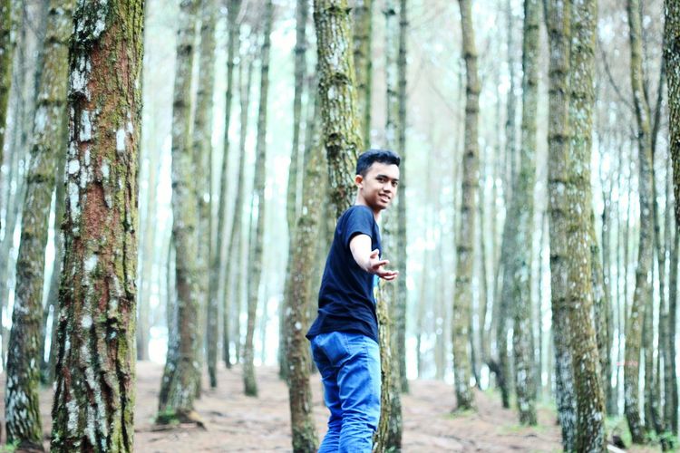 Portrait of young man standing on tree trunk