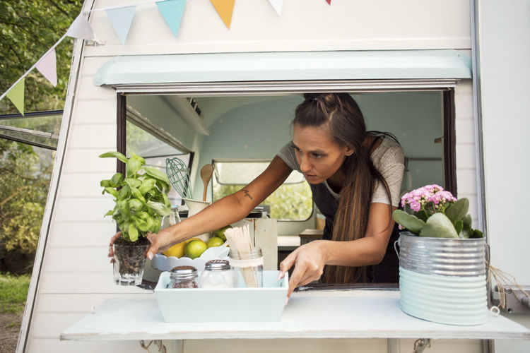 Female owner arranging potted plant on window at food truck
