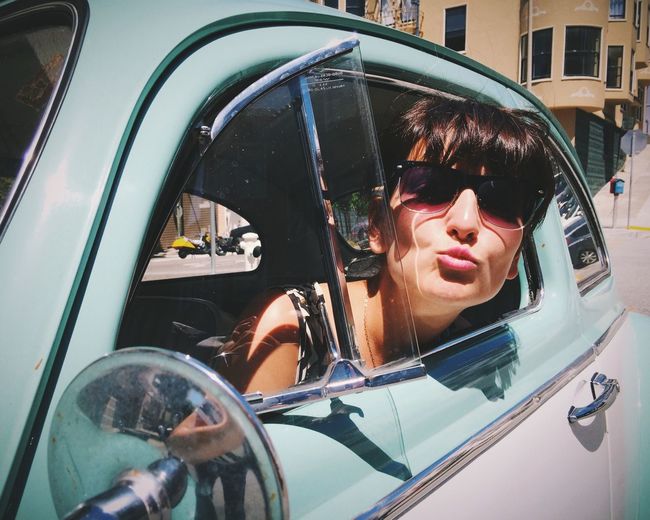 Portrait of young woman puckering lips while peeking from car window
