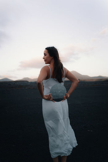 Young woman standing on land against sky during sunset