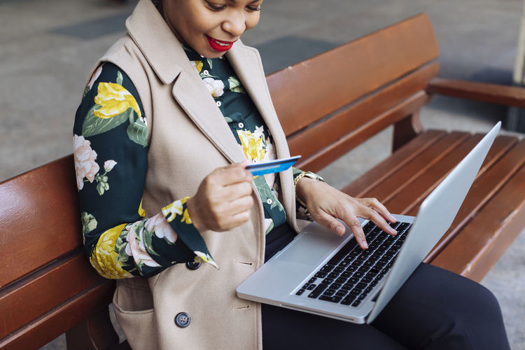 Businesswoman sitting on bench using laptop and credit card