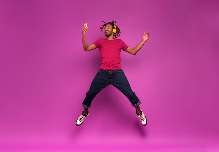 Full length of  man jumping against pink background