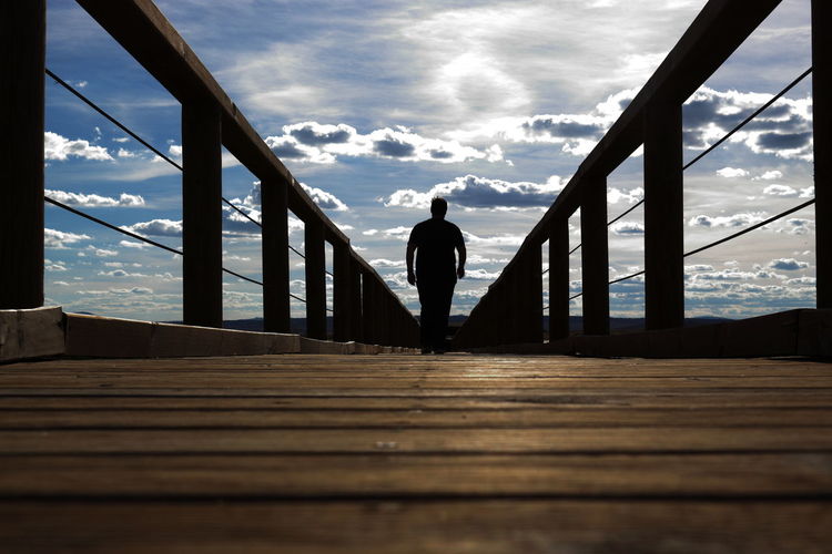 Rear view of man standing on footbridge against sky