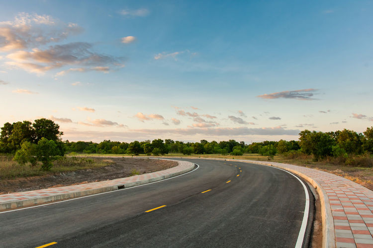 Road by trees against sky during sunset