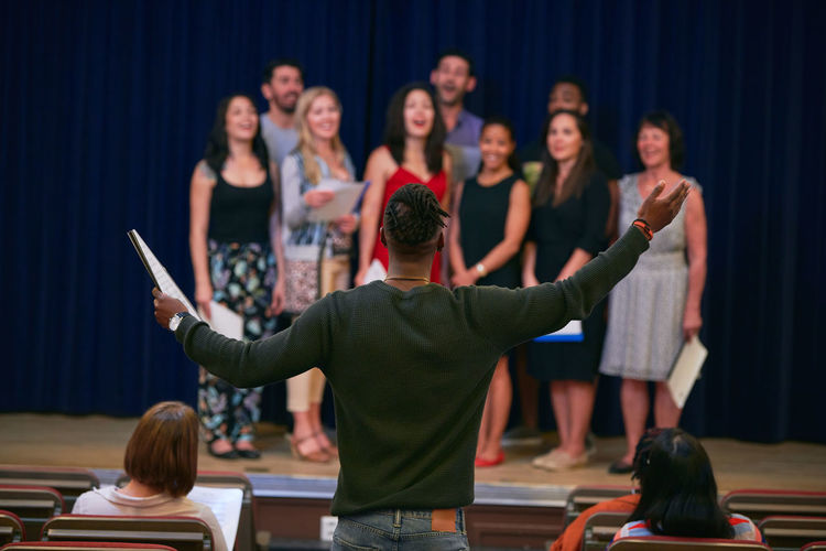 Conductor leading choir on stage in auditorium