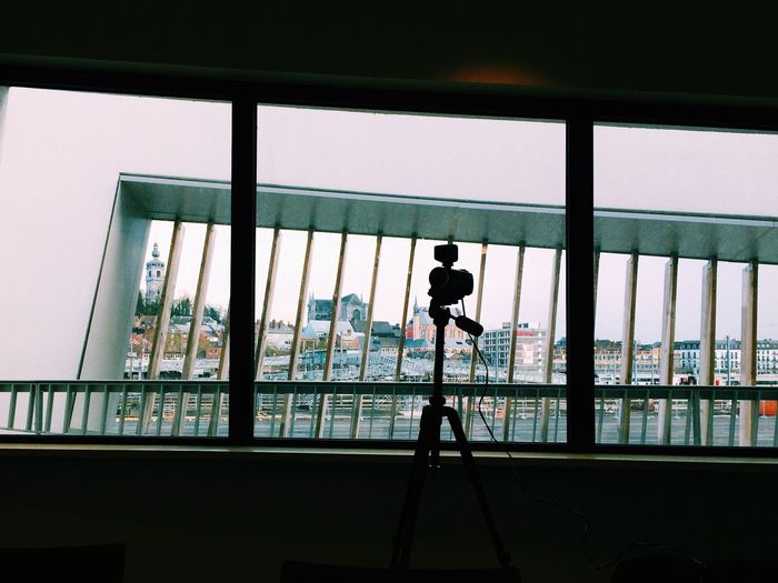 Silhouette video camera on tripod by window glass