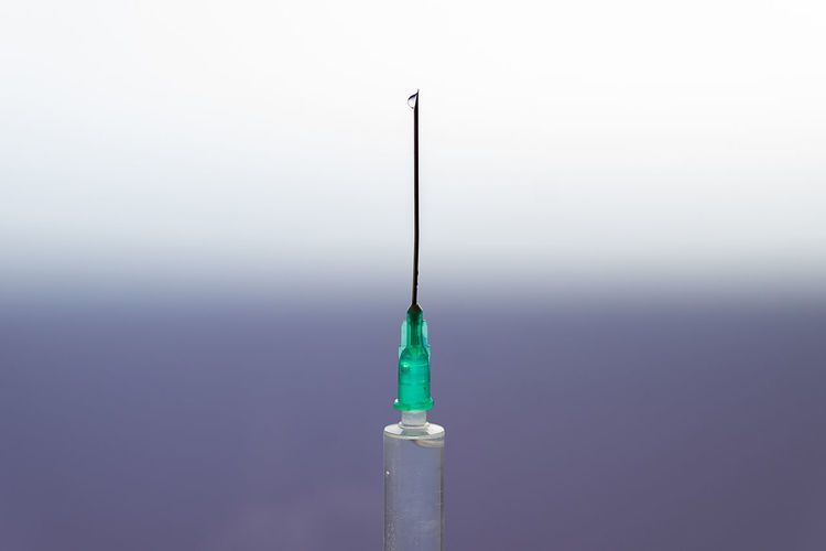 Closeup of sterile syringe with drop of remedy on needle on blurred gradient background