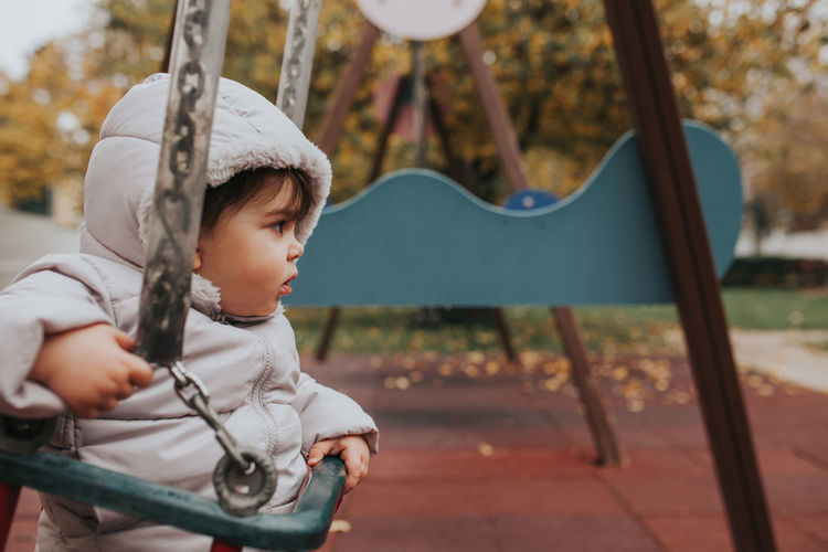 Baby girl sitting on swing at playground