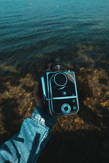 Man holding camera while standing by sea