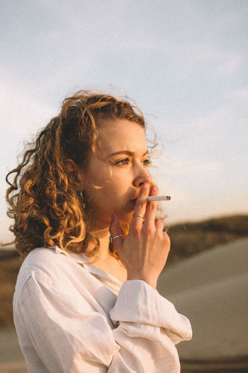 Close-up of woman smoking cigarette against sky