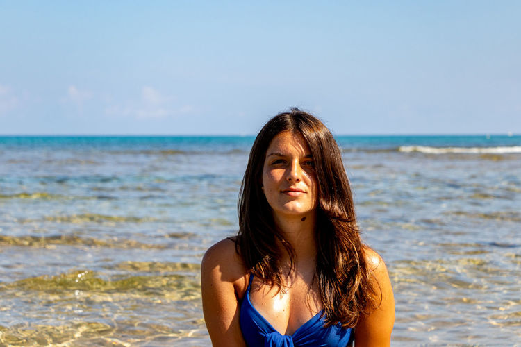 Beautiful young woman at beach against sky