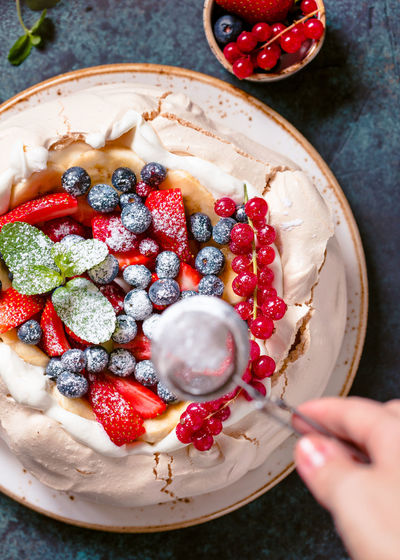 Cropped hand of woman sprinkling powdered sugar in bowl on table