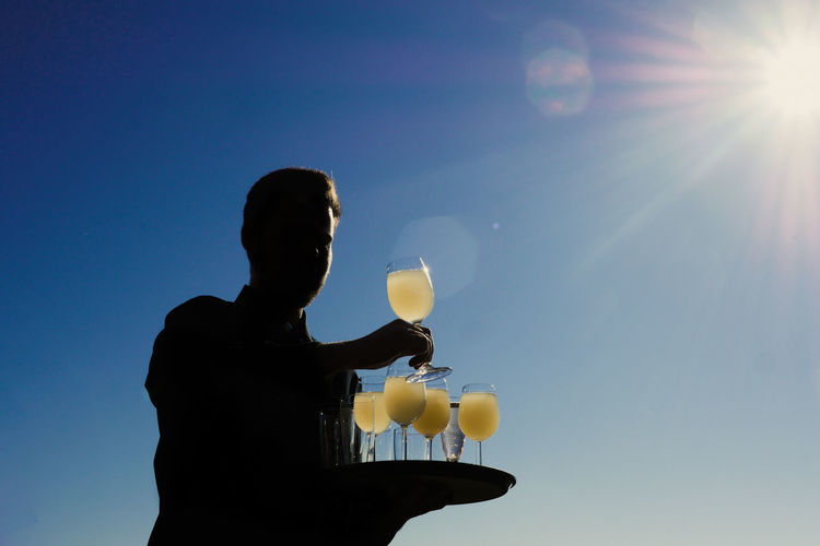 Low angle view of silhouette woman holding glass against blue sky