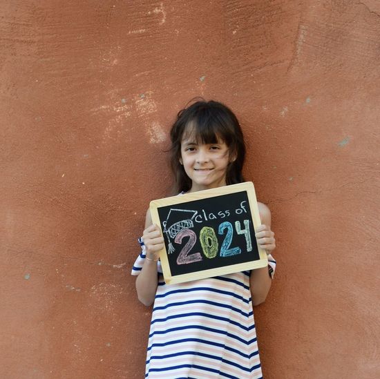 Portrait of smiling girl with message standing against brick wall