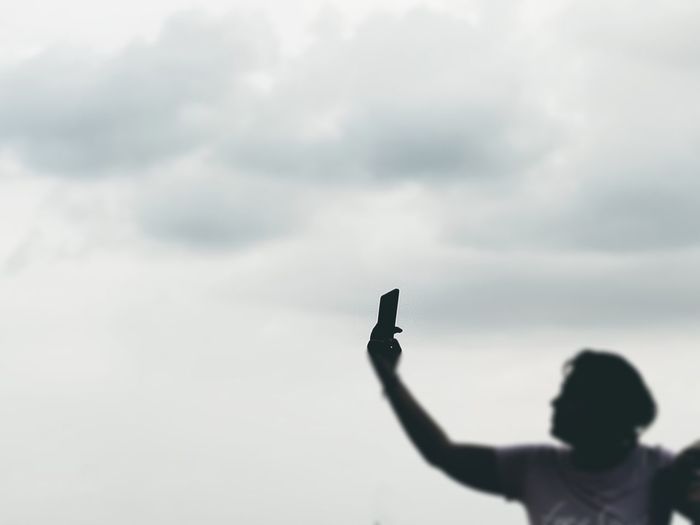 Man taking with arms raised taking selfie on mobile phone against sky