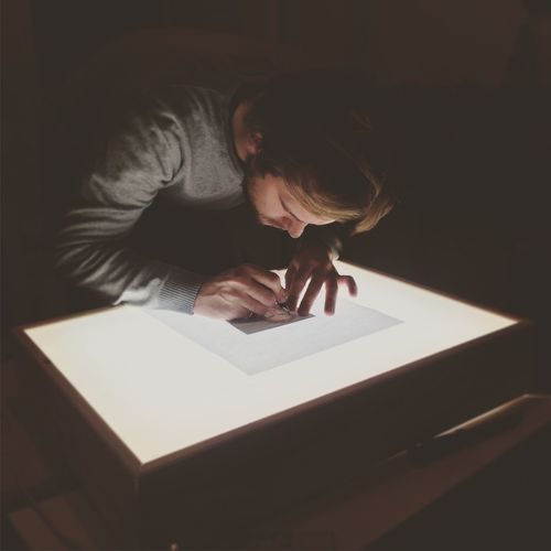 Close-up of man drawing against table light