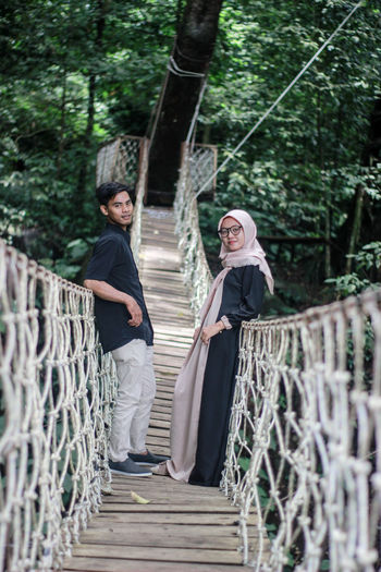 Portrait of couple standing on footbridge in forest
