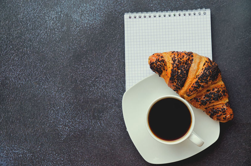 Businessman working morning with notebook, cup of hot coffee and sweet croissant on black background