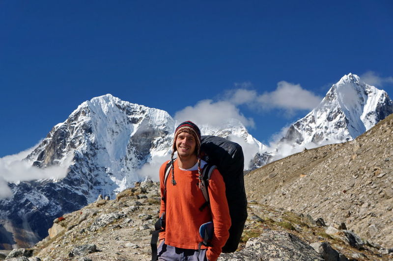 A smiling tourist with a backpack stands on a white mountains backdrop.