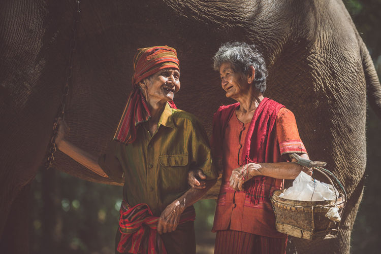 Senior couple standing by elephant in forest
