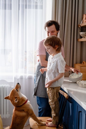 Family fun in the kitchen. cute little boy making whipped cream with his dad and furry friend
