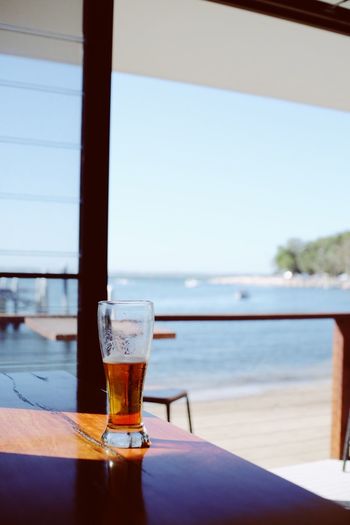 Glass of beer on table by sea against clear sky
