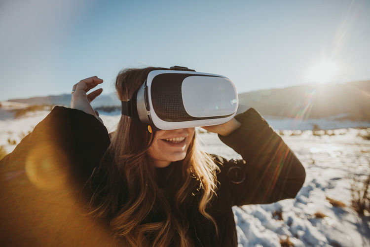 Smiling woman using vr while standing on snow covered land