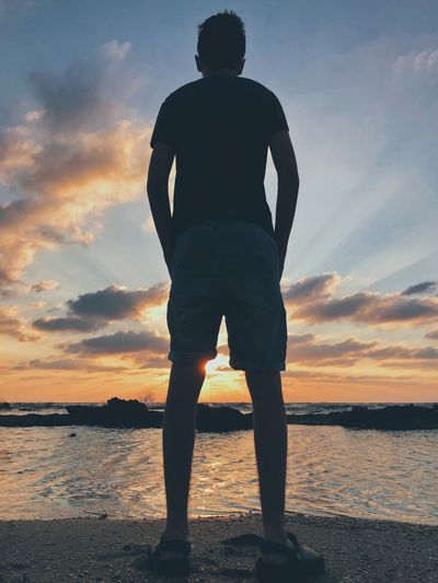 Rear view of man looking at sea against sunset sky