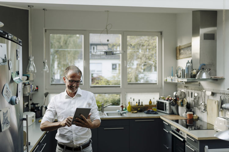 Mature man using digital tablet while standing in kitchen at home