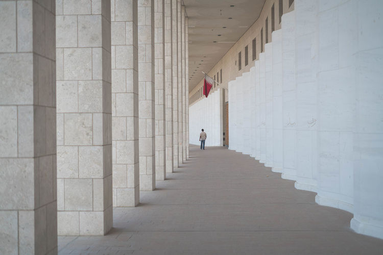 REAR VIEW OF MAN WALKING ON BUILDING CORRIDOR
