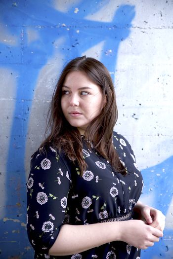 Woman looking away while standing against blue graffiti wall