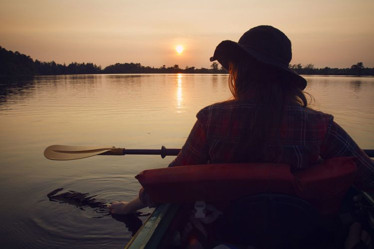 Rear view of woman kayaking in lake at forest during sunset