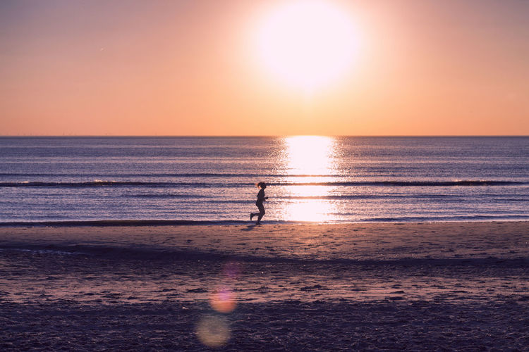 Silhouette woman running at beach against sky during sunset