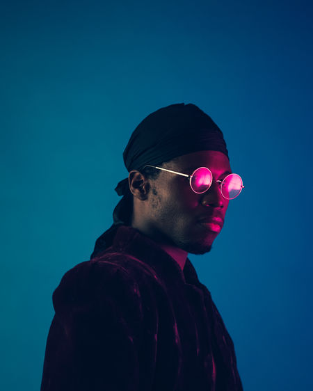 Portrait of young man wearing sunglasses against blue background