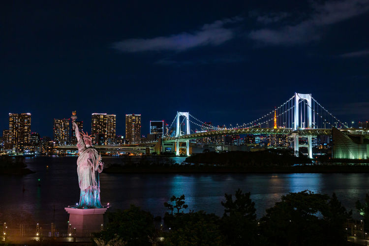 View of rainbow bridge and statue of liberty in odaiba, japan at night