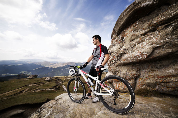Male athlete with bicycle standing on mountain against sky