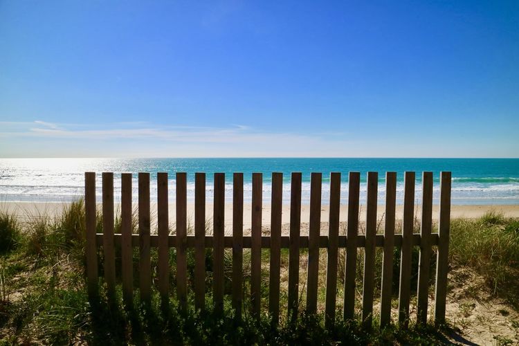 Fence at beach against blue sky during sunny day