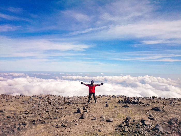 Rear view of man standing cliff against cloudy sky