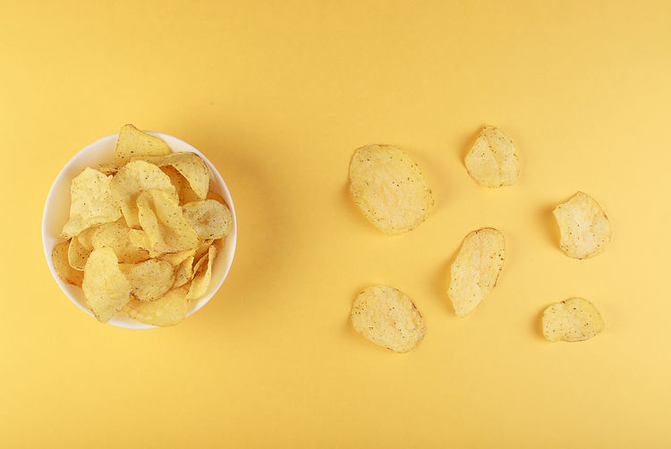 Crispy potato chips in bowl on yellow background, top view