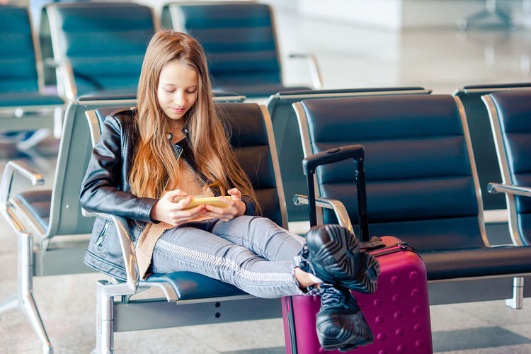 Girl using mobile phone while sitting at airport
