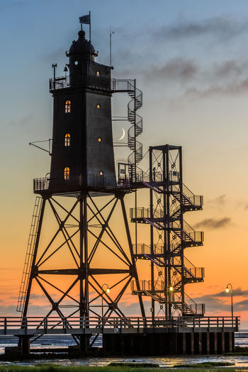 Lighthouse at beach against sky during sunset