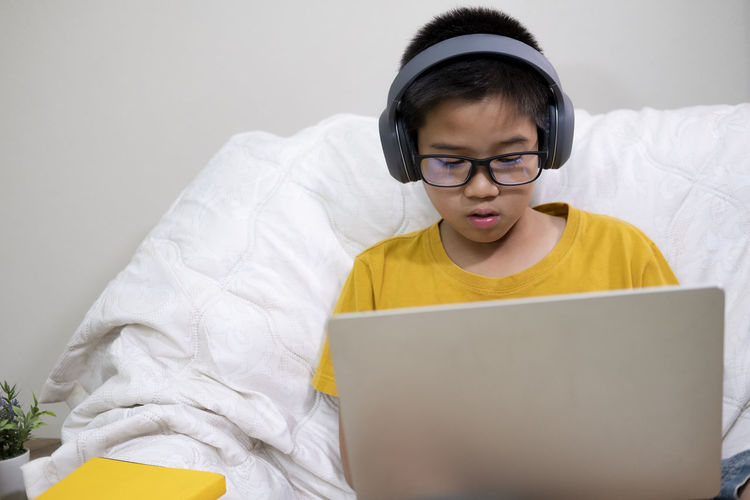 Boy using laptop while sitting on bed